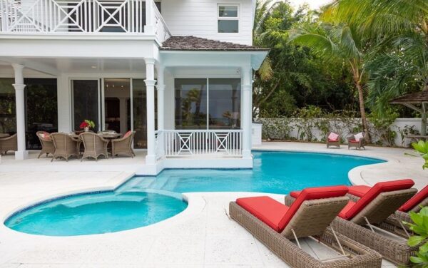 a pool area with two chairs outside a house